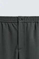 Pantalón regular fit color marrón oscuro, confeccionado en tejido con viscosa. Cuenta con cintura elástica, bolsillos delanteros y detalle de bolsillos traseros de vivo. El cierre frontal es con cremallera y botón.
