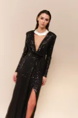 Vestido largo de lentejuelas color negro, con escote profundo en V, mangas largas y tajo lateral en la falda. Presenta un diseño cruzado con fruncido en la cintura y espalda elastizada.