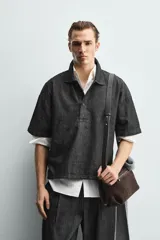 Camisa de manga corta con cuello solapa y cierre frontal de botones. Confeccionada en tejido denim de algodón, de corte relajado y aberturas laterales en el bajo.