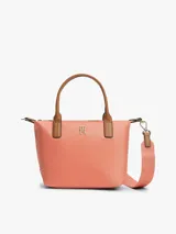 Cartera tote Tommy Hilfiger de nailon color salmón, con dos asas superiores de cuero sintético marrón y correa tejida extraíble. Cuenta con cierre de cremallera y detalle del monograma TH en metal dorado en la parte delantera.