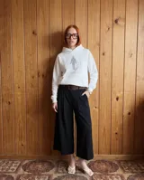 Canguro oversize blanco con capucha y bolsillo frontal tipo canguro. Presenta un estampado gráfico central con una figura humana esquemática y líneas curvas en color violeta, acompañado de la inscripción 'FIG. 1 LOS DE AFUERA SON DE PALO'.