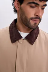 Campera color taupe de corte recto, con cuello camisero de pana marrón oscuro, cierre frontal oculto con botones a presión y grandes bolsillos frontales con solapa.