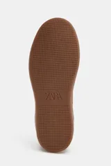 Zapatillas deportivas de caña baja con combinación de colores y materiales. El cuerpo principal es de color bordó, con refuerzos en gamuza marrón y detalles en color crema. La suela es de goma marrón. El cierre es mediante cordones gruesos color crema.