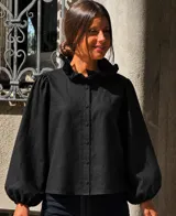 Camisa de lino color negro con cuello alto con volados, cierre frontal de botones y mangas largas abullonadas con puños ajustados.