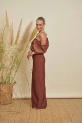 Vestido largo color marrón de corte recto, con escote profundo adornado con pedrería brillante. Presenta un diseño de hombros descubiertos con mangas voluminosas tipo lazo o drapeado, confeccionado en tela satinada.