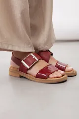 Sandalias de cuero marrón, con diseño de dos fajas amplias, una lisa en la parte delantera y otra superior con hebilla metálica grande y ajustable. Suela plana con plataforma baja y pespunte visible.