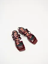 Sandalias de cuero con acabado charol color bordó, con punta cuadrada, tiras onduladas en el empeine y correa ajustable con hebilla en el tobillo. Cuentan con un taco bajo forrado.
