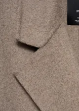 Abrigo largo de diseño oversize con tejido de lana, cuello con solapas de muesca y cierre frontal de doble botonadura. Presenta hombros caídos, manga larga y dos bolsillos laterales, con una abertura posterior en el bajo.