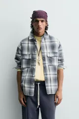 Camisa de algodón de corte relajado, con cuello solapa, manga larga terminada en puño con botón y dos bolsillos de plastrón con solapa en el pecho. Presenta un estampado de cuadros en tonos azules, grises y blancos, y cierre frontal de botonadura.