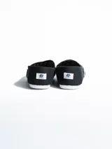 Alpargata de lona negra con suela de goma blanca flexible. Presenta una etiqueta pequeña con el logo de la marca en el lateral y plantilla interior de símil cuero.