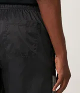 Bermuda deportiva de tejido plano de poliamida, color negro y gris claro, con bloques de color reflectivo en la parte inferior. Presenta cintura elástica con amarre y un pequeño logo de la NASA en la pierna derecha.