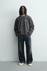 Sudadera de corte relajado confeccionada en tejido de algodón con textura acanalada. Presenta cuello redondo, manga larga y un diseño con efecto lavado. Incluye un texto estampado en contraste en la parte frontal.