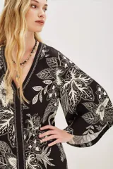 Vestido largo negro con estampado floral en color crema, escote en V y mangas acampanadas.