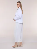 Camperita corta de calce recto color blanco, confeccionada en tejido liviano con textura arrugada. Cuenta con cuello con solapa, diseño estampado sobre los hombros y canesú, cierre frontal con botones de madera rústicos, bolsillos superiores en el pecho con solapa y mangas largas con puño abotonado.