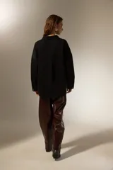 Sobrecamisa de jean color negro, con cierre frontal de botones metálicos, mangas largas y detalle de pequeñas tachas decorativas en la parte superior delantera.