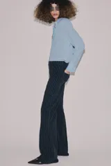 Jeans de tiro alto con corte flare y diseño de rayas verticales. Presenta cintura con trabillas, falsos bolsillos delanteros con solapa y botón, y cierre frontal con cremallera y botón.