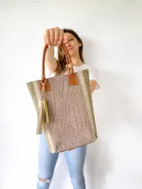Bolso tote de cuero color taupe con textura croco y detalles en verde. Tiene doble asa de mano de cuero marrón y un dije de cuero con flecos. No tiene división interna.
