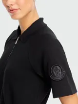 Vestido negro de algodón con cuello polo, cierre frontal con cremallera, mangas cortas, cintura ajustable con cordón y bolsillos laterales.