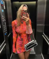 Vestido corto de microtul elastizado con estampado floral en tonos naranja, rosa y negro. Tiene cuello alto y mangas largas acampanadas.