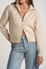 Cardigan de punto acanalado en color beige melange con motas oscuras. Presenta un diseño ajustado al cuerpo, cierre frontal completo con cremallera metálica y cuello alto.