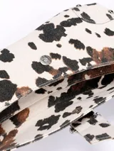 Cartera baguette con estampado de vaca en blanco y negro, con correa de hombro y cierre con hebilla metálica.