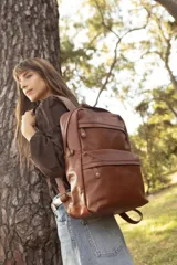 Mochila de cuero marrón, con compartimento principal amplio, bolsillo frontal con cierre y tiradores metálicos. Cuenta con correas regulables y diseño apto para notebook.
