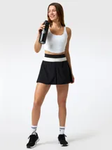 Falda pantalón deportiva de color negro con pretina ancha tejida en franjas blanca y negra, diseño plisado al frente y shorts internos.