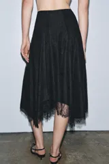 Falda midi negra de tiro medio, confeccionada en tejido de encaje con forro interior a tono. Presenta un bajo asimétrico con terminación en línea evasé y cierre lateral oculto.
