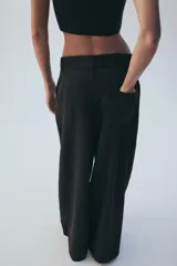 Pantalón de tiro medio color marrón, con pinzas en el delantero, perneras anchas de corte recto y trabillas para cinturón. Cuenta con bolsillos laterales y traseros, y cierre frontal con cremallera y botón.
