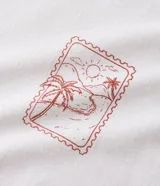 Musculosa blanca de algodón, de corte comfort y cuello redondo. Presenta un estampado localizado en el pecho con un diseño de palmeras y un atardecer en tonos rosados y naranjas.