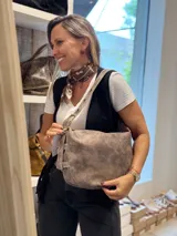 Bolso tipo hobo de cuero con acabado desgastado en tono visón. Presenta una correa ajustable con hebilla metálica y diseño de estructura redondeada.