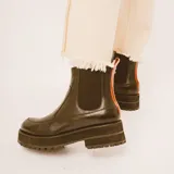 Botas negras de cuero estilo chelsea, con suela track gruesa y elásticos laterales. Presentan una tira vertical de cuero marrón en la parte posterior.