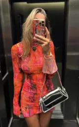 Vestido corto de microtul con estampado abstracto en tonos naranja y fucsia. Tiene cuello alto, mangas largas acampanadas y abertura lateral en la falda.