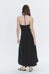Vestido largo de color negro con cuello halter y escote recto. Presenta un diseño fluido con cierre de cremallera oculta en la espalda y lazada ajustable en el cuello.
