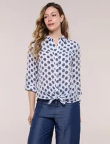 Camisa de gasa blanca con estampado de lunares en tonos azules, cuello con solapa, cierre frontal de botones, bolsillo aplicado en el pecho y detalle de nudo en el dobladillo inferior. Cuenta con mangas largas regulables.