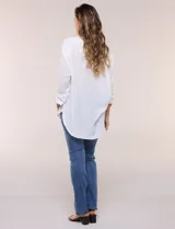 Camisa Magaschoni de silueta holgada y tejido texturizado color blanco, con cuello camisero, cierre frontal de botones, mangas largas con presilla para arremangar y diseño asimétrico con espalda más larga.