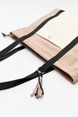 Bolso tipo tote de nylon negro con bolsillo frontal en color crema y asas largas en cinta gris. Cuenta con cierre superior y diseño funcional de gran capacidad.