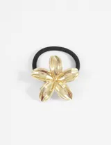 Gomita para el pelo con elástico negro y aplique metálico en forma de flor de hibisco color dorado.