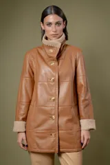 Campera de cuero color tostado con diseño de paneles, cuello alto y puños con forro de corderito sintético. Presenta cierre frontal con botones grandes y bolsillos laterales.