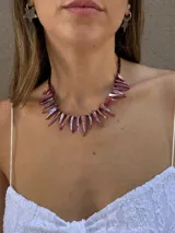 Collar corto con bastones de nácar teñidos en tonos rosados iridiscentes y mostacillas. Se cierra con cadena de acero quirúrgico y gancho para regular el largo.