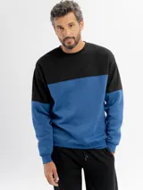 Buzo de felpa con diseño de bloques de color, combinando negro en la parte superior y azul en la parte inferior y mangas. Presenta cuello redondo y puños elásticos.