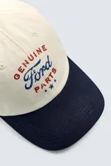 Gorra de seis paneles, color beige, con visera azul marino. Presenta bordado frontal con el texto "Genuine Ford Parts" en tonos azul y rojo, y un pequeño parche bordado con el logo de Ford en el lateral.