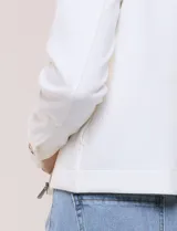 Camperita corta blanca de punto elastizado, con cuello camisero, cierre frontal completo y mangas largas con puños anchos abotonados.