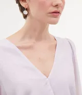 Blusa Cortelle de manga larga en color lila, confeccionada en 100% poliéster. Presenta diseño cruzado (transpasse), escote en V profundo, mangas abullonadas semitransparentes con puños elásticos.