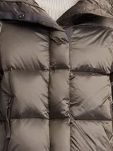 Campera puffer larga color oliva con capucha, cierre frontal con botones a presión y bolsillos laterales con cierre. Diseño acolchado con relleno de plumas.