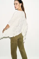 Top de cuello redondo color celeste con textura fruncida, mangas tipo capa y bajo asimétrico.