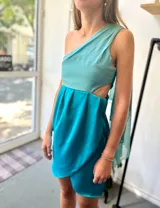 Vestido corto turquesa de un hombro con volado de gasa y corte en la cintura.