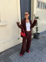 Conjunto de dos piezas compuesto por un blazer y un pantalón de corte sastrero, confeccionados en tela de algodón con estampado de rayas verticales blancas sobre fondo gris. El blazer presenta solapas clásicas y cierre frontal, mientras que el pantalón es de tiro medio y pierna recta.