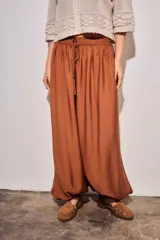 Babucha de viscosa color ladrillo, de tiro alto con cintura elástica fruncida y cordón ajustable del mismo tejido, con diseño fluido y puños ajustados en los tobillos.