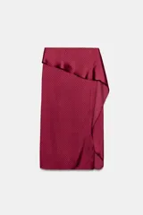 Falda midi de tiro medio confeccionada en tejido satinado con estampado de lunares. Presenta un diseño envolvente con detalle de volante lateral y cierre posterior con cremallera oculta.